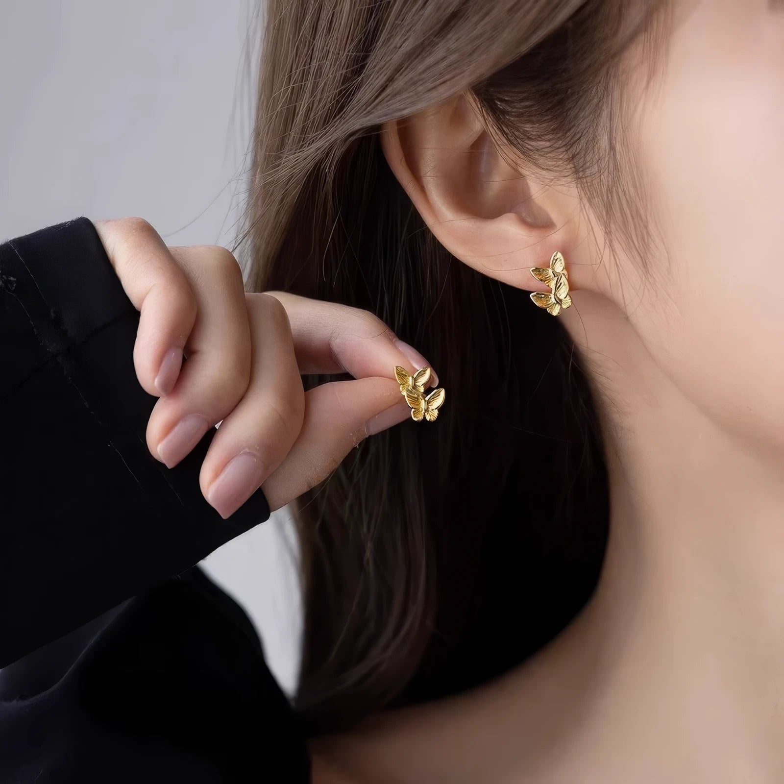 Hand holding a gold butterfly stud earring, with one earring worn