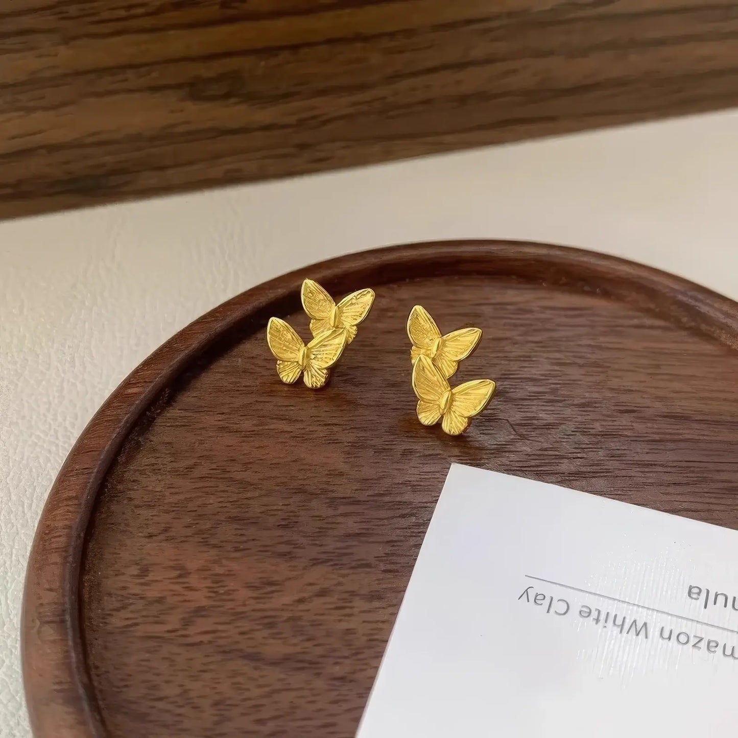 Gold butterfly stud earrings placed on a wooden plate