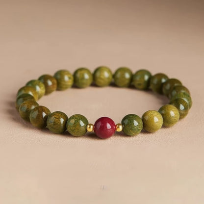 Green sandalwood bead bracelet with a cinnabar bead and gold - toned spacer, placed on a light - colored surface.