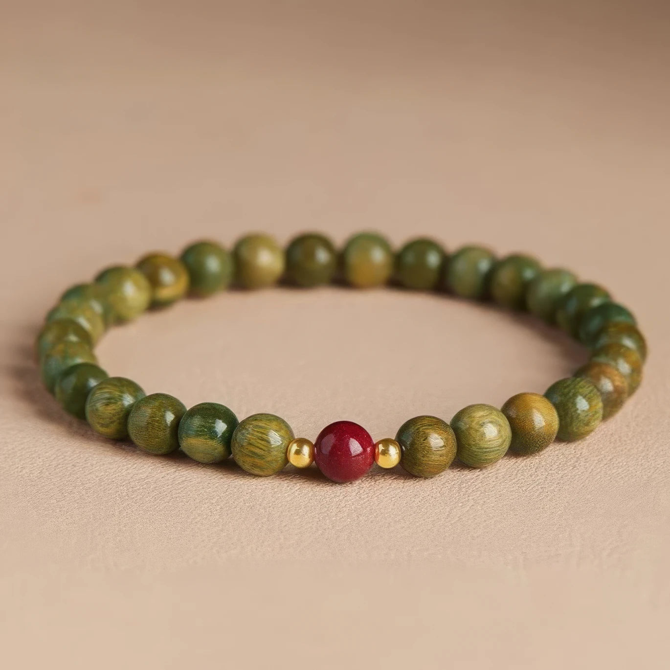 Green sandalwood bead bracelet with a cinnabar bead and gold - toned spacer, another view on a light - colored surface.