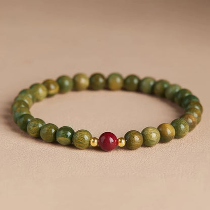 Green sandalwood bead bracelet with a cinnabar bead and gold - toned spacer, another view on a light - colored surface.