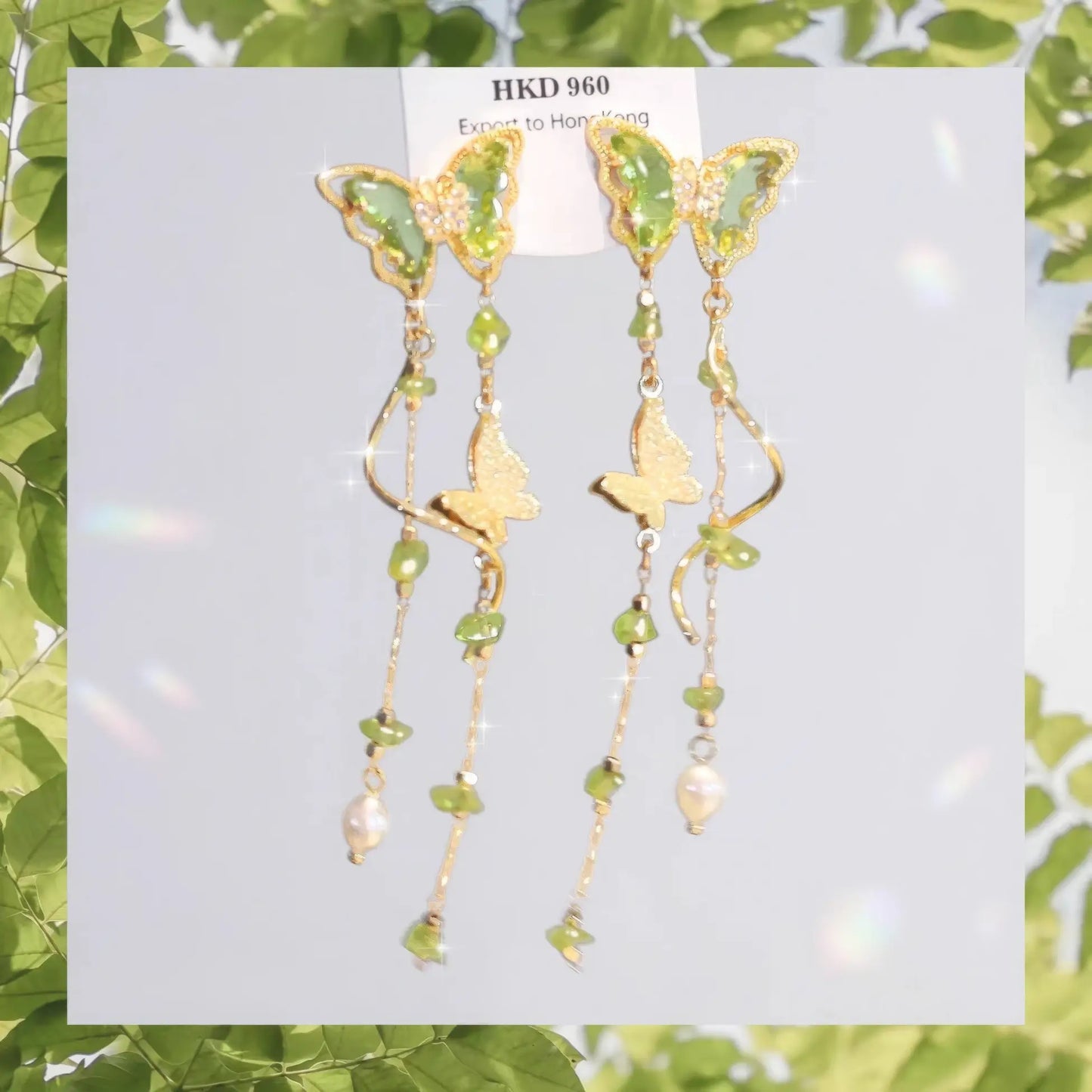 A pair of Green Wild Tea Butterfly Tassel Earrings showcased on a card with a green leafy border.