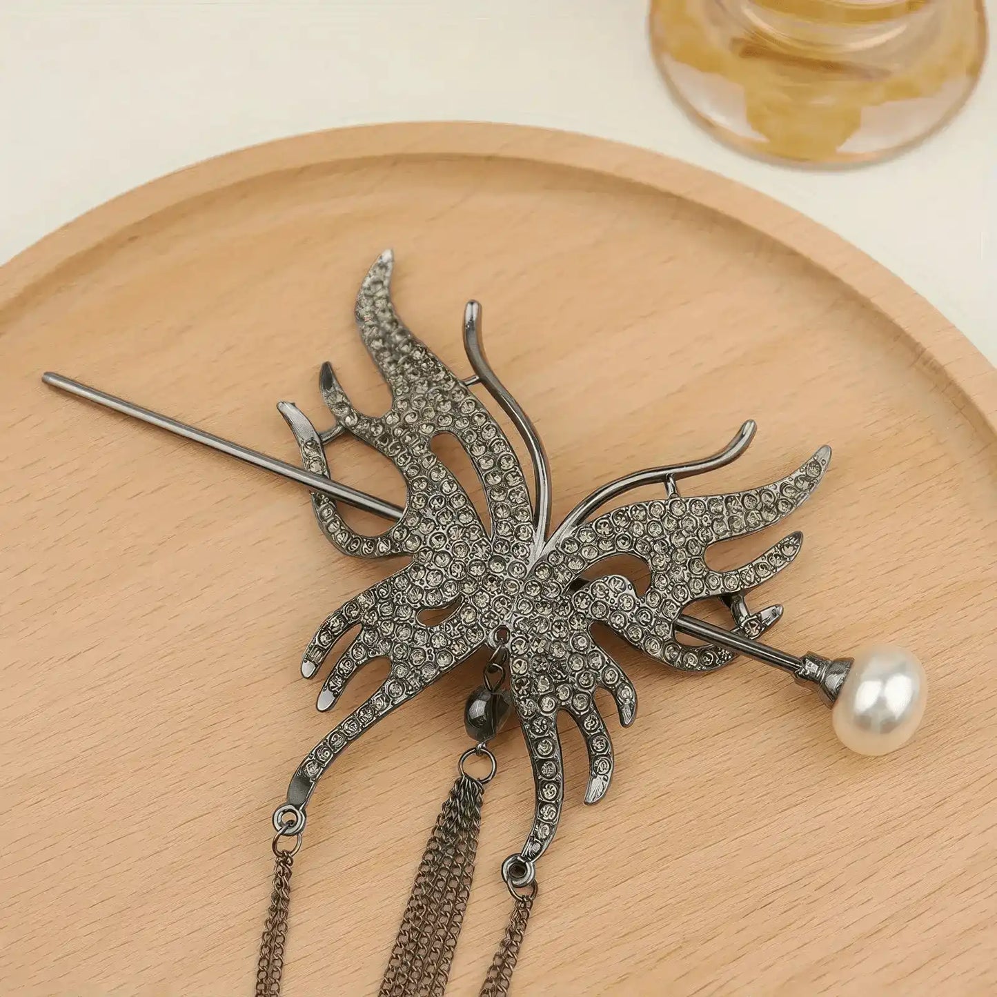 Dark gunmetal rhinestone butterfly tassel hairpin set with matte dark metal texture and layered tassels, laid flat on light wooden round tray for texture showcase.