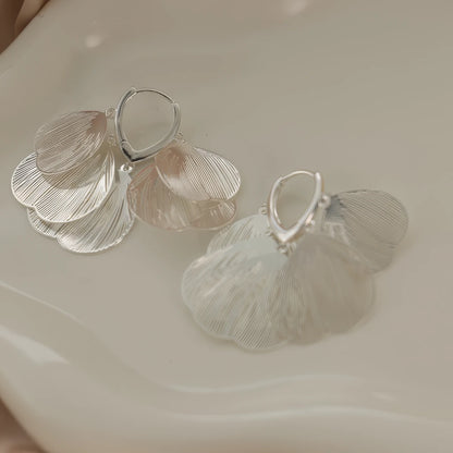 Silver hollow petal - shaped tassel earrings, displayed on a curved surface, emphasizing the detailed, layered petal design