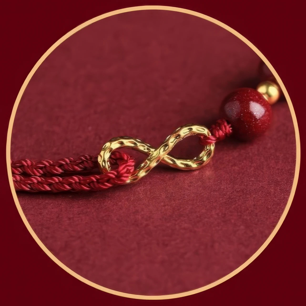 Close - up of the gold "infinite" symbol on a red string bracelet, on a red background.
