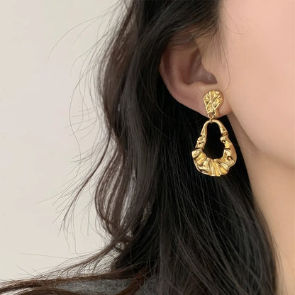 Irregular - shaped gold earrings worn, complementing dark hair, showcasing the bold and textured design