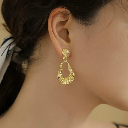  Irregular - shaped gold earrings worn, paired with a tied - back hairstyle, emphasizing the unique, open - drop structure