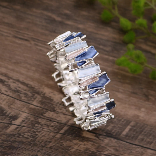  Irregular colorful enamel bracelet isolated on a wooden surface with green plants in the background.