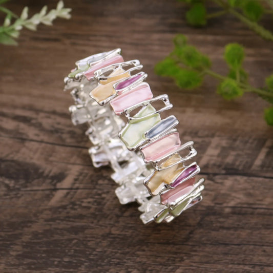Irregular colorful enamel bracelet isolated on a wooden surface with green plants in the background.