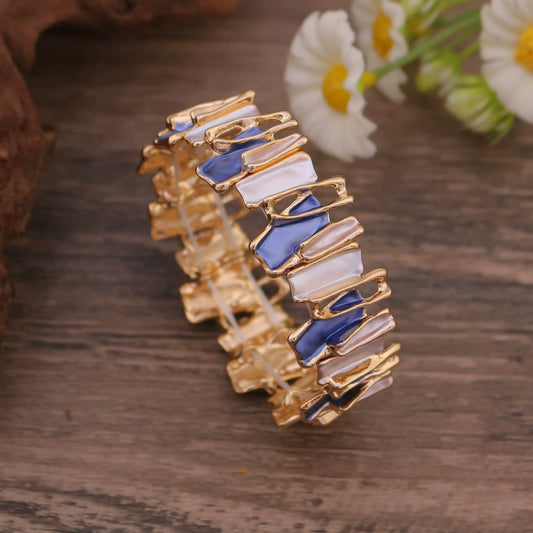 Irregular colorful enamel bracelet placed on a wooden surface with a daisy in the background.