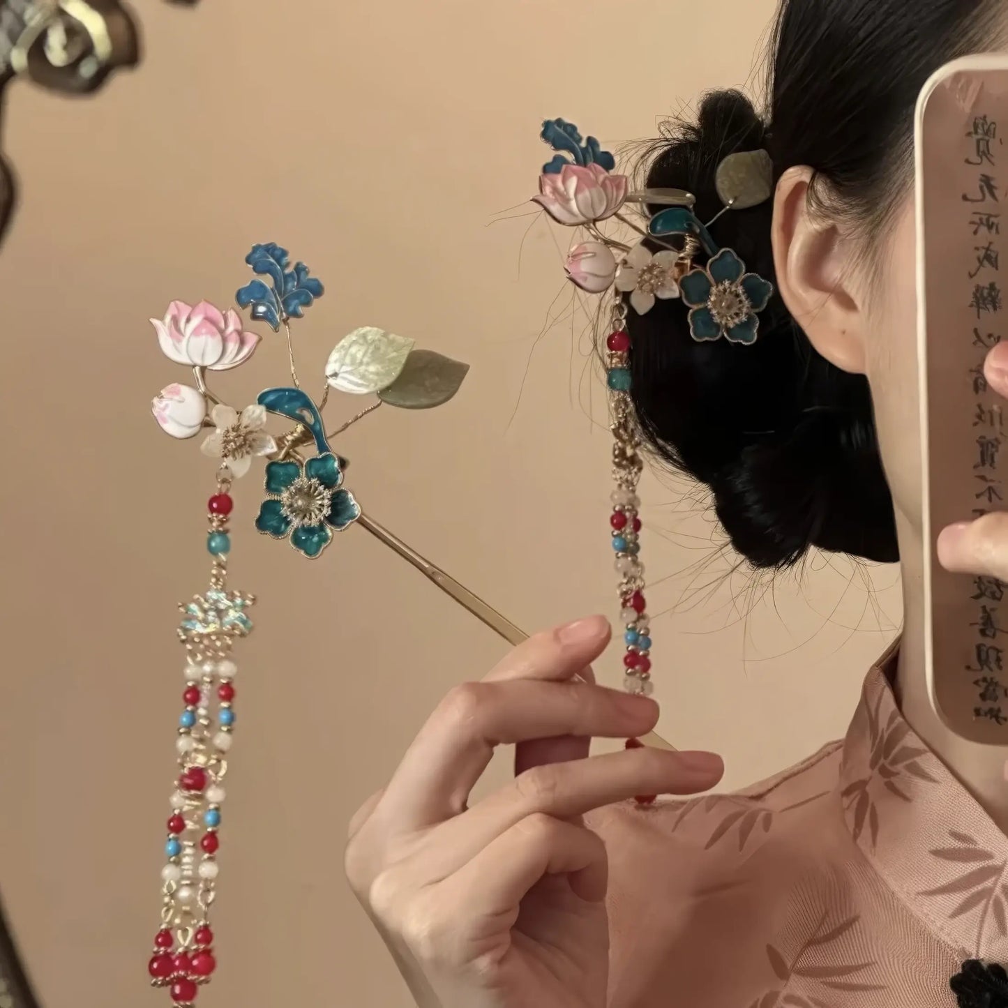 Mirror selfie of the hairpin being adjusted in a traditional bun, showing both the floral top and tassel from the side.