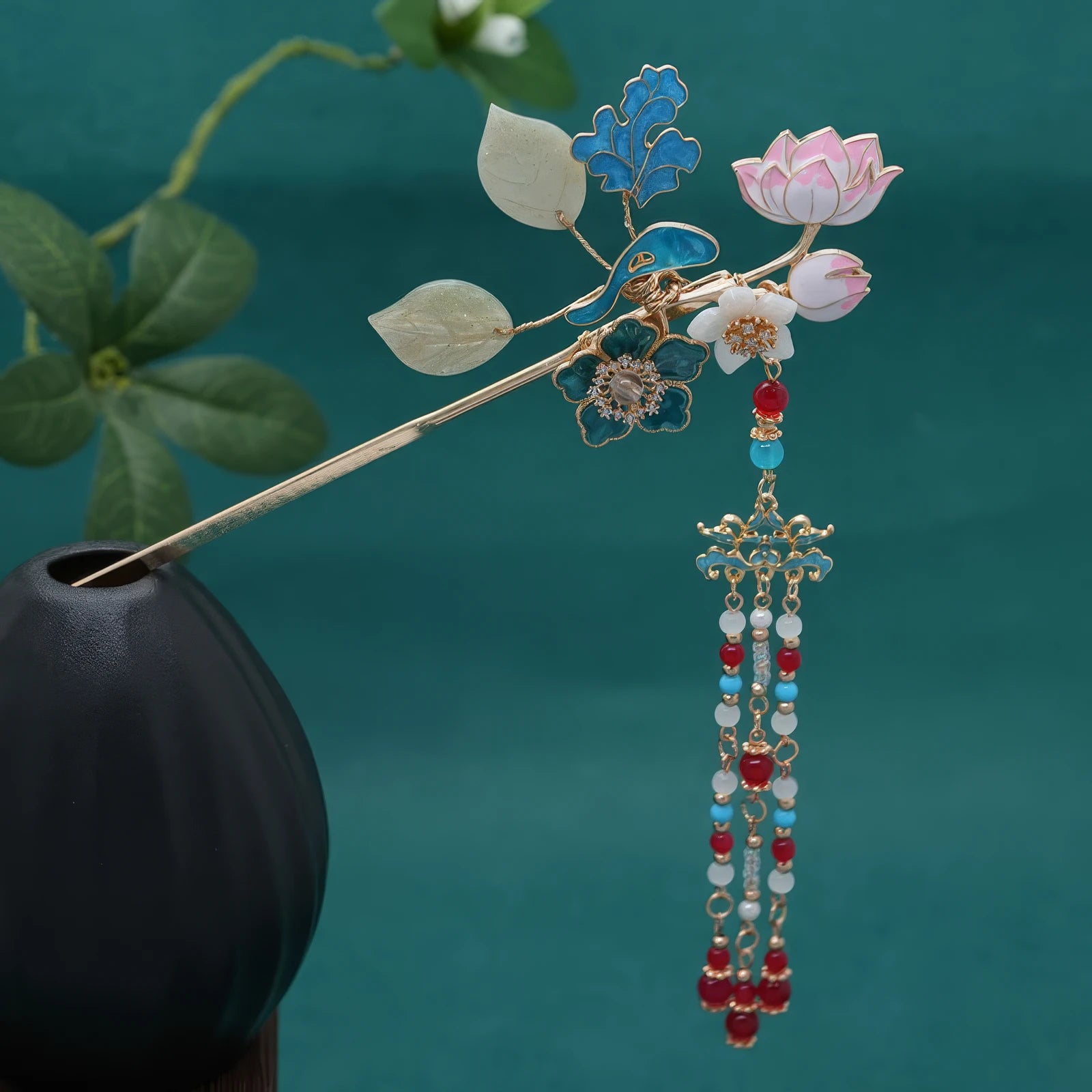 Hairpin inserted into a black vase, with the full tassel hanging down against a teal background, showing the complete length of the beaded drops.