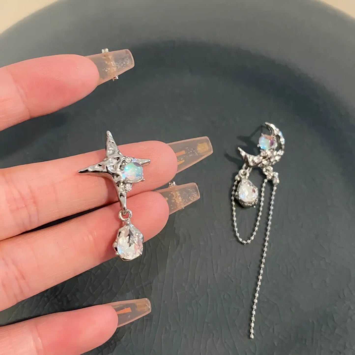  Hand holding moon and star asymmetric zircon earrings over a dark - colored surface, displaying the intricate design.