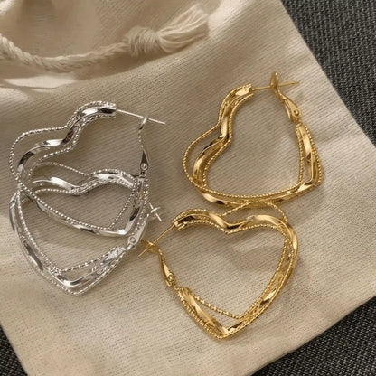 Mixed gold and silver multi - layered heart earrings, displayed on fabric, emphasizing the variety of metallic tones
