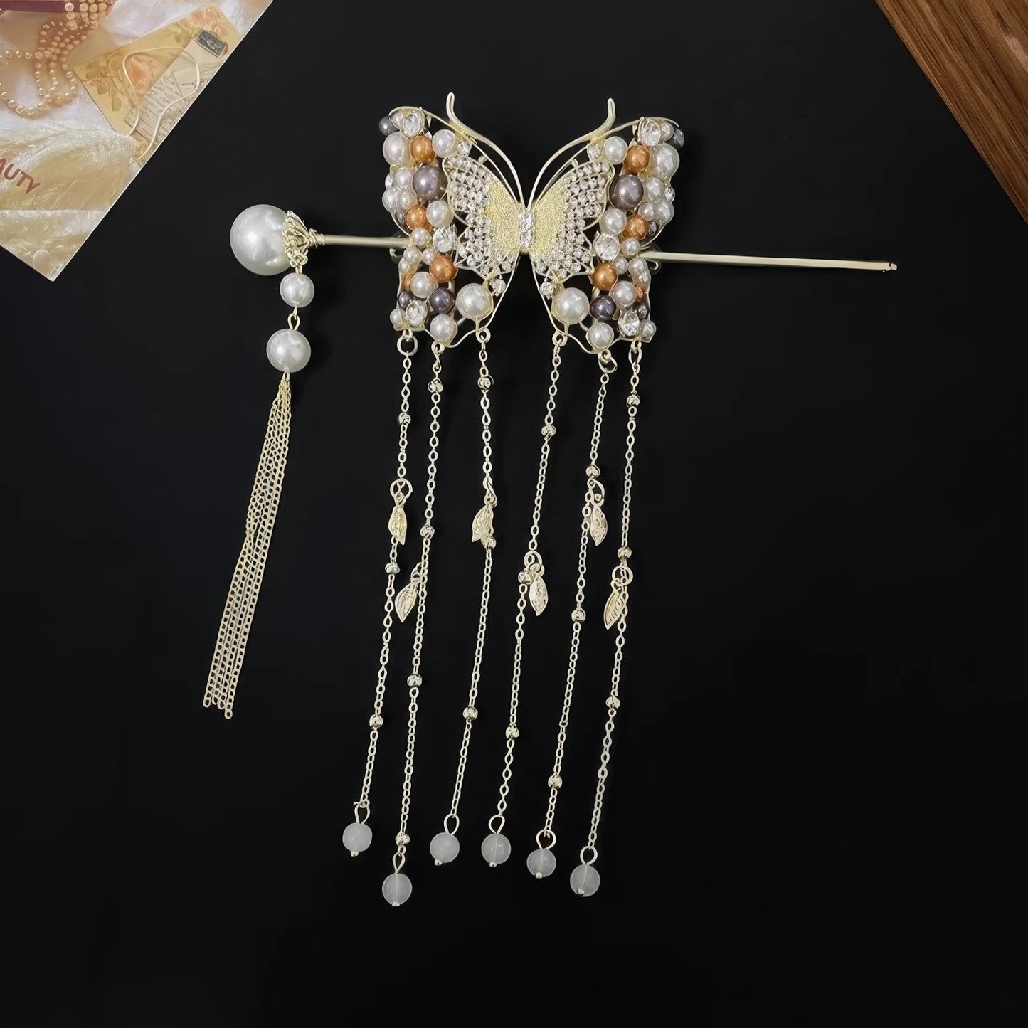 Golden crystal butterfly hairpin with multi-layer pearl tassels matched with a separate pearl tassel hair stick, laid flat on textured background to show complete set design.