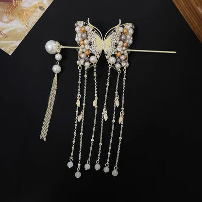 Golden crystal butterfly hairpin with multi-layer pearl tassels matched with a separate pearl tassel hair stick, laid flat on textured background to show complete set design.