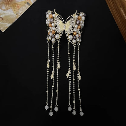 Single golden butterfly hairpin embedded with crystals and pearls, with dense multi-strand pearl tassels, displayed flat on textured light background.