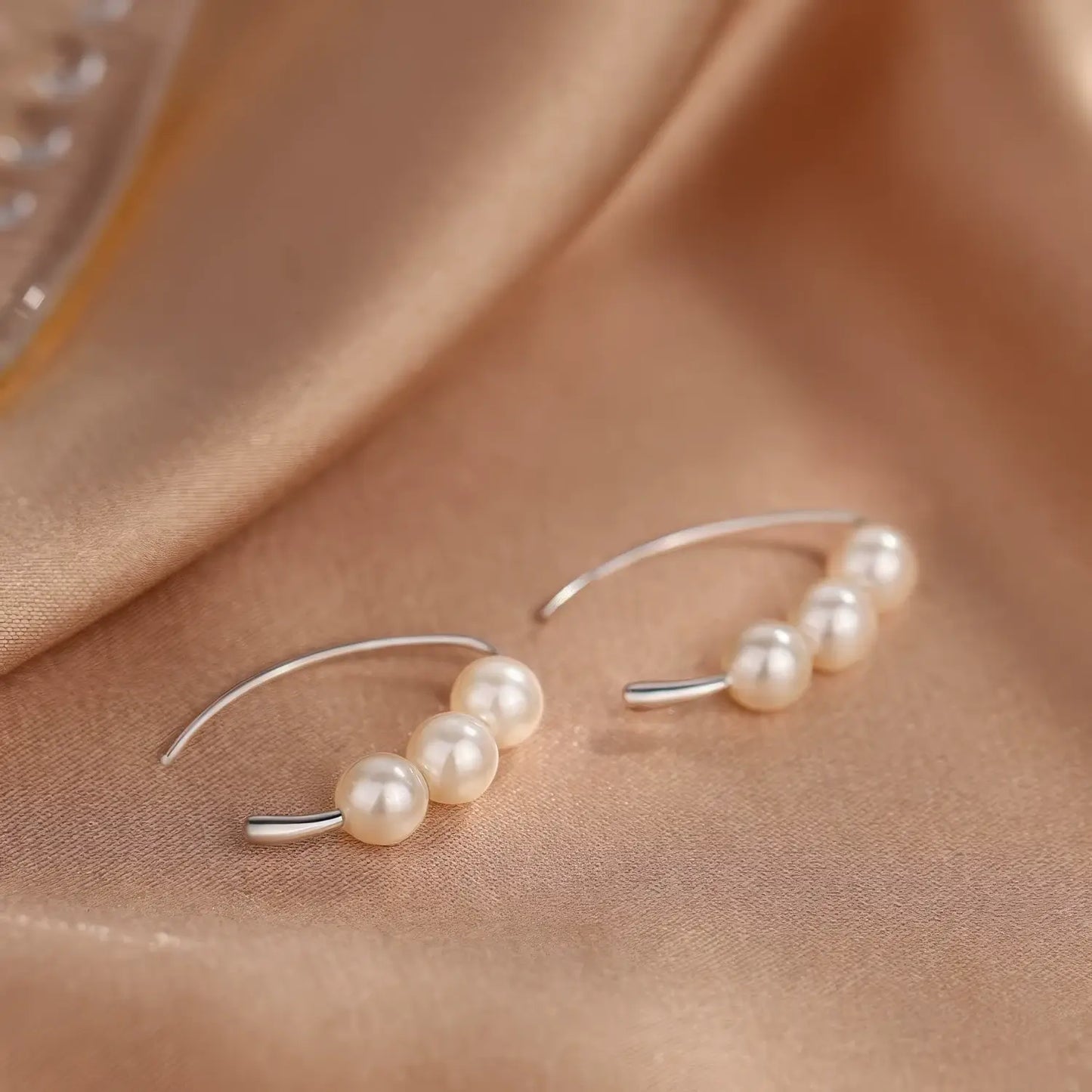 Silver - toned pearl hoop earrings displayed on satin fabric, emphasizing the curved shape and clustered pearls
