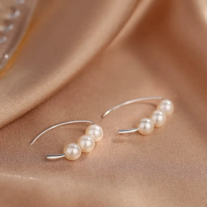Silver - toned pearl hoop earrings displayed on satin fabric, emphasizing the curved shape and clustered pearls