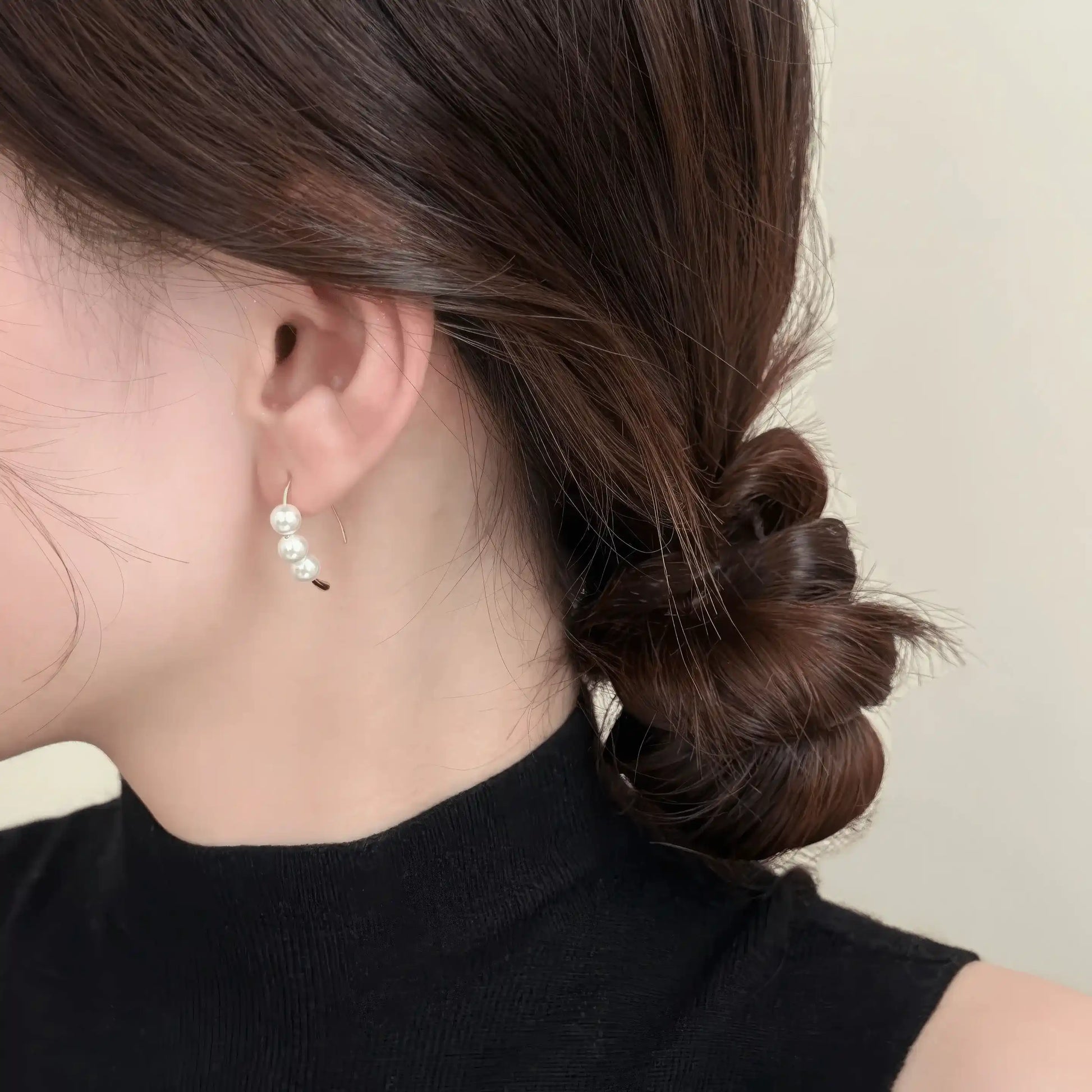 Pearl hoop earrings worn, complementing a bun hairstyle, highlighting the delicate clustered pearl design