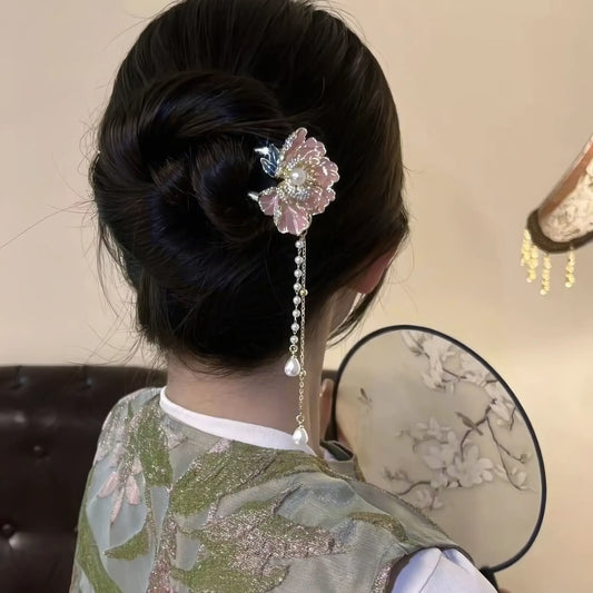 Back view of the peony flower hairpin paired with a green brocade top, with a decorative fan visible, highlighting the hairpin's tassel and delicate floral details.