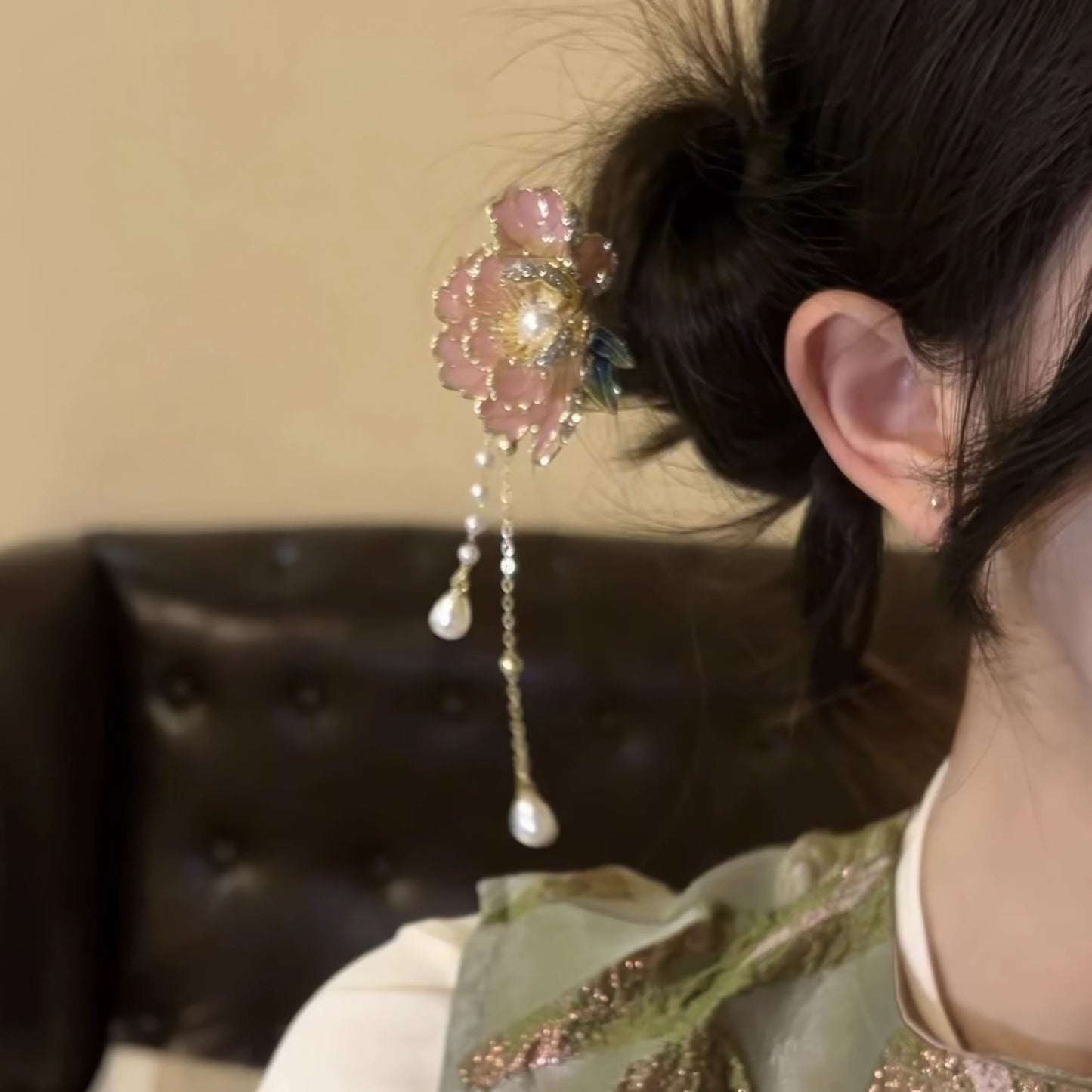 Side view of the peony flower hairpin clipped into a messy bun, showcasing the pink peony bloom, metallic accents, and layered pearl tassels against a dark background.