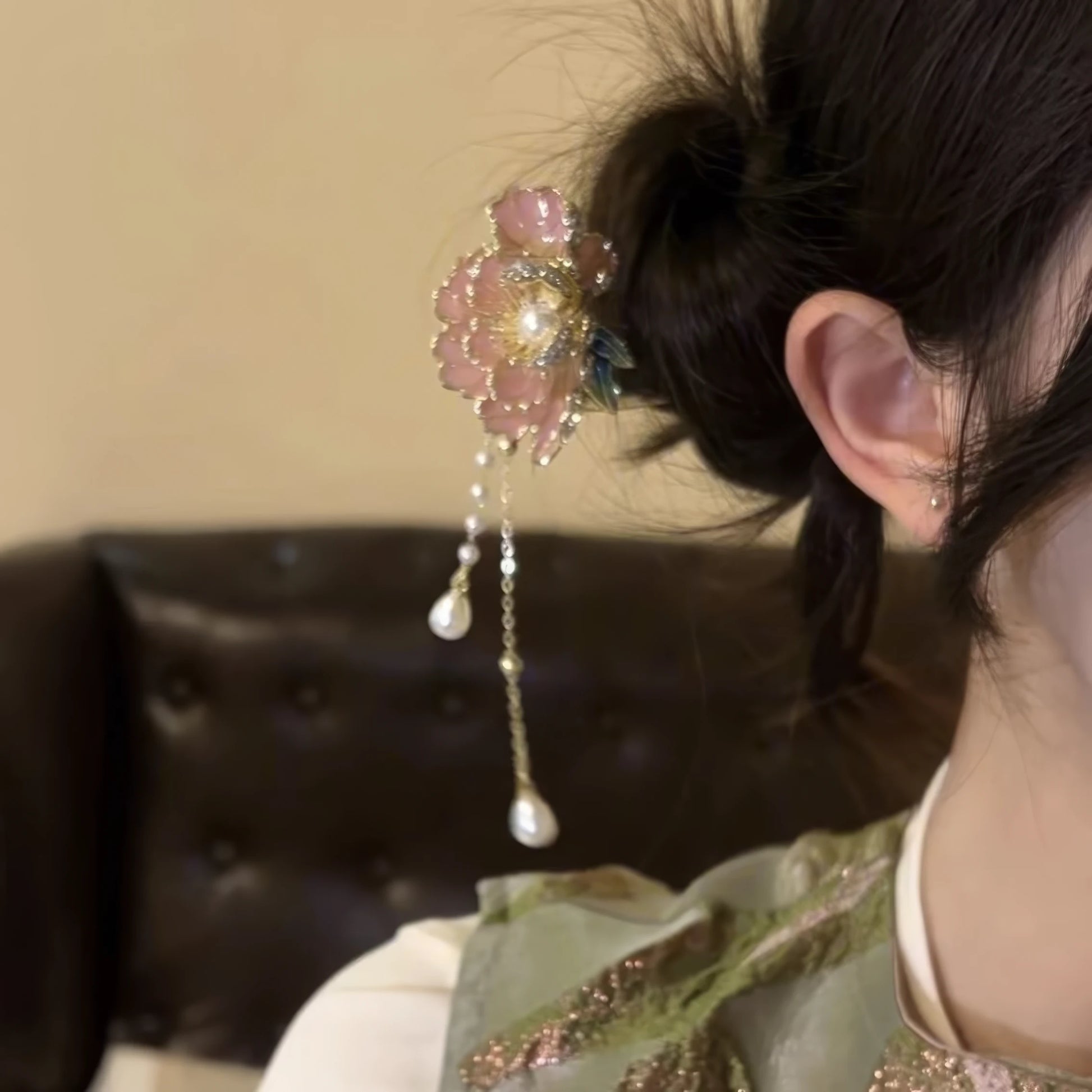 Side view of the peony flower hairpin clipped into a messy bun, showcasing the pink peony bloom, metallic accents, and layered pearl tassels against a dark background.
