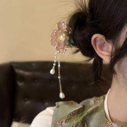 Side view of the peony flower hairpin clipped into a messy bun, showcasing the pink peony bloom, metallic accents, and layered pearl tassels against a dark background.