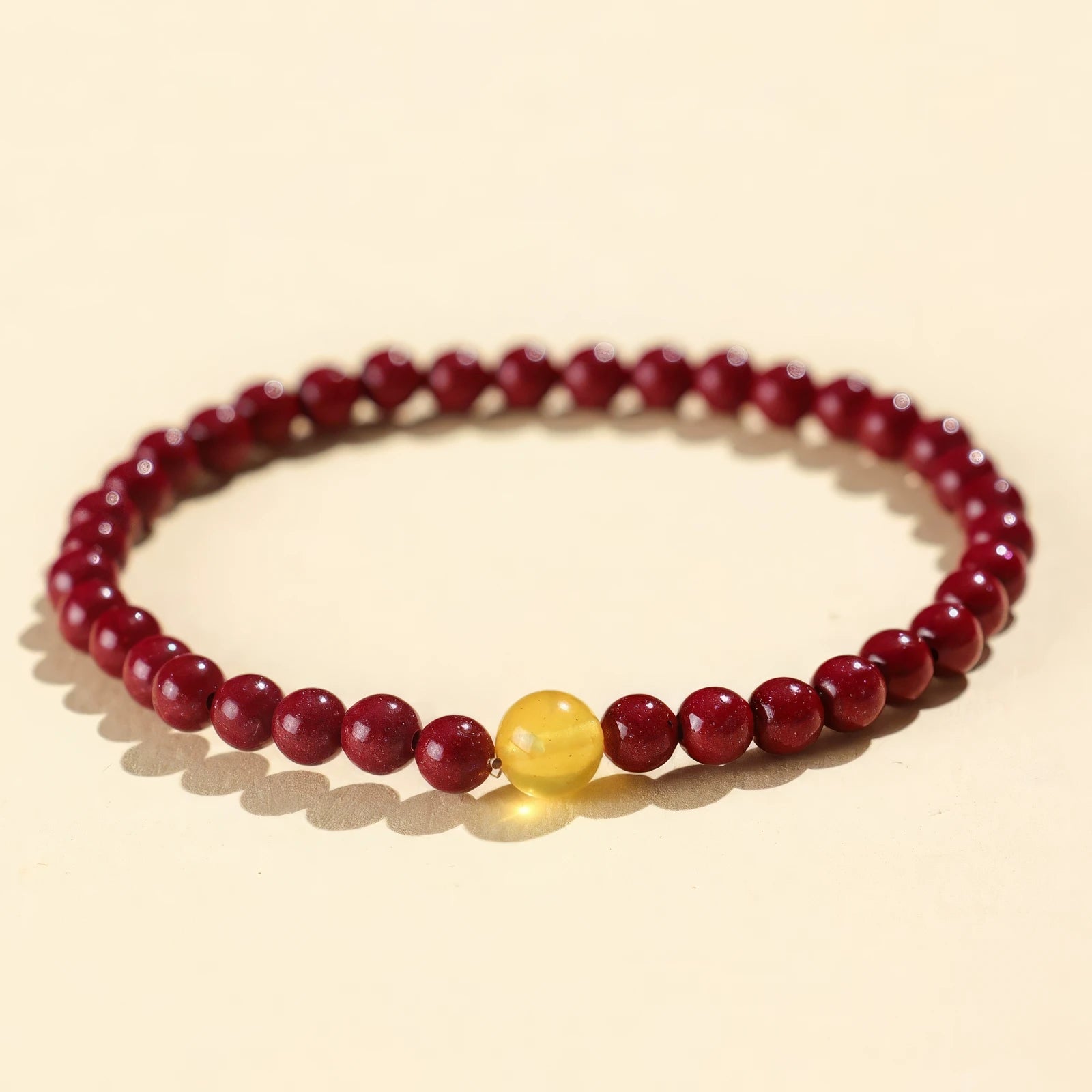 Purple gold cinnabar bead bracelet with a yellow bead accent, isolated on a light - colored background.