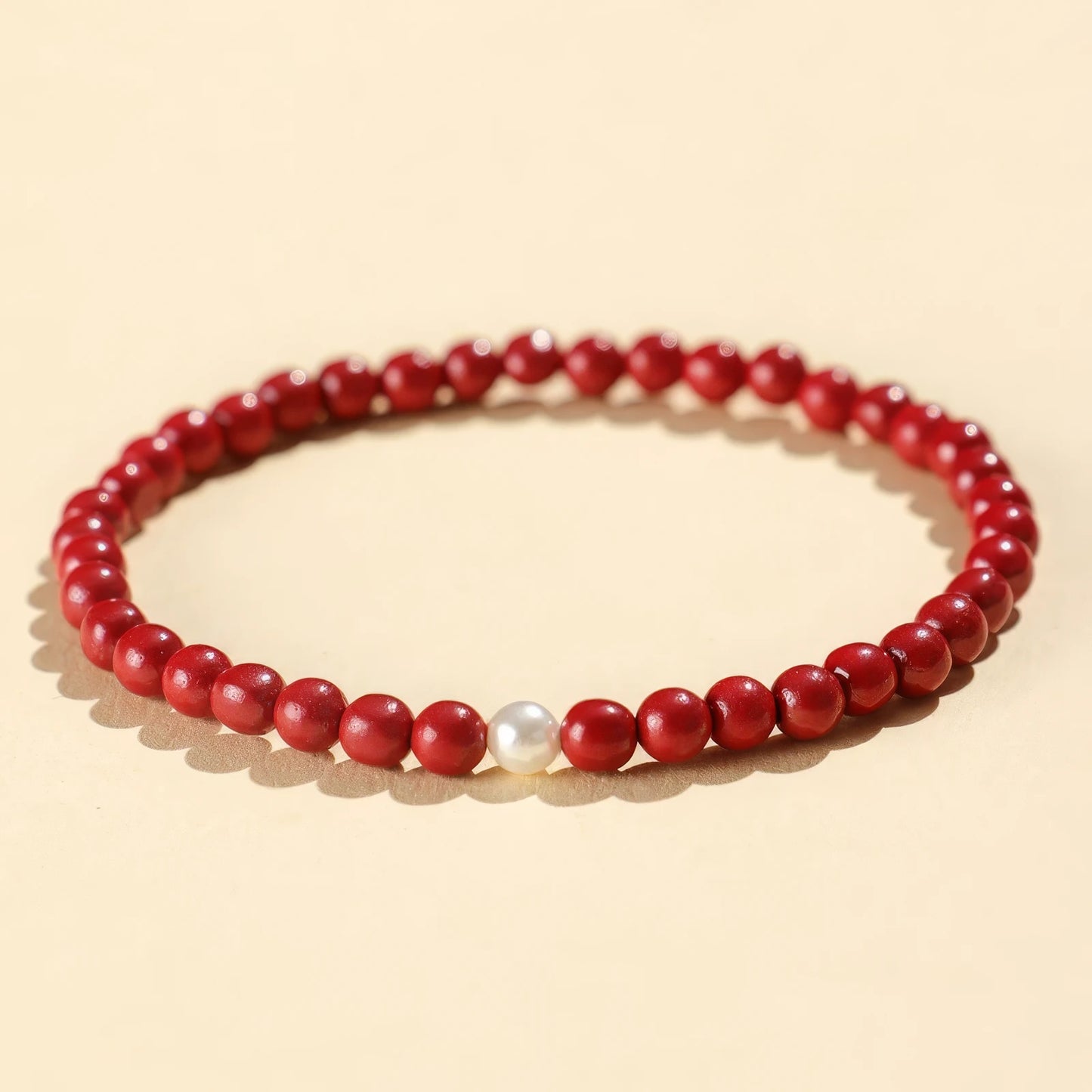 Purple gold cinnabar bead bracelet featuring a single pearl, isolated on a light - colored background.