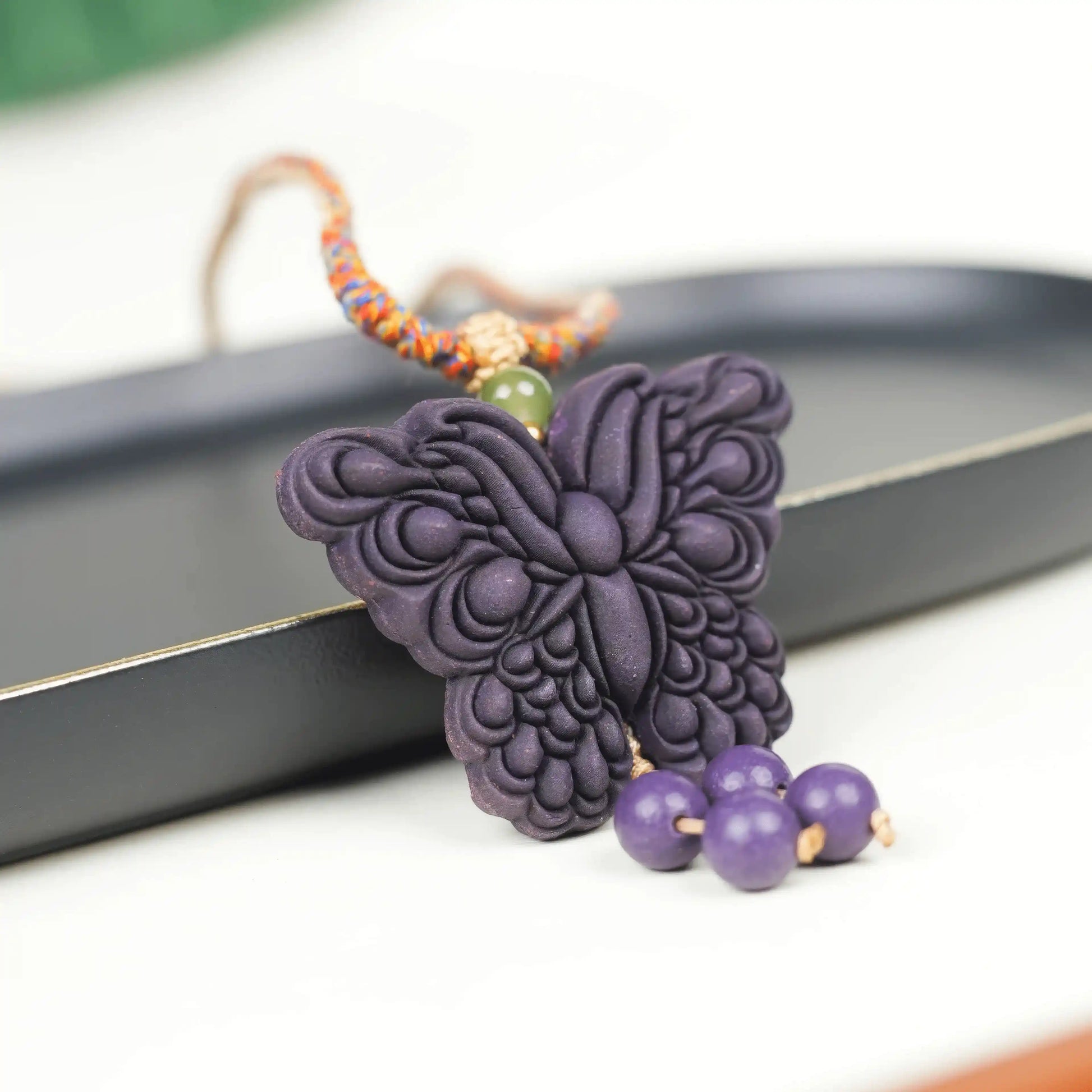 Close-up of the "Purple Qi Coming from the East - Double-Sided Butterfly Incense Pendant" placed on a black tray, with a vivid and lifelike butterfly shape and hanging beads adding a sense of agility.