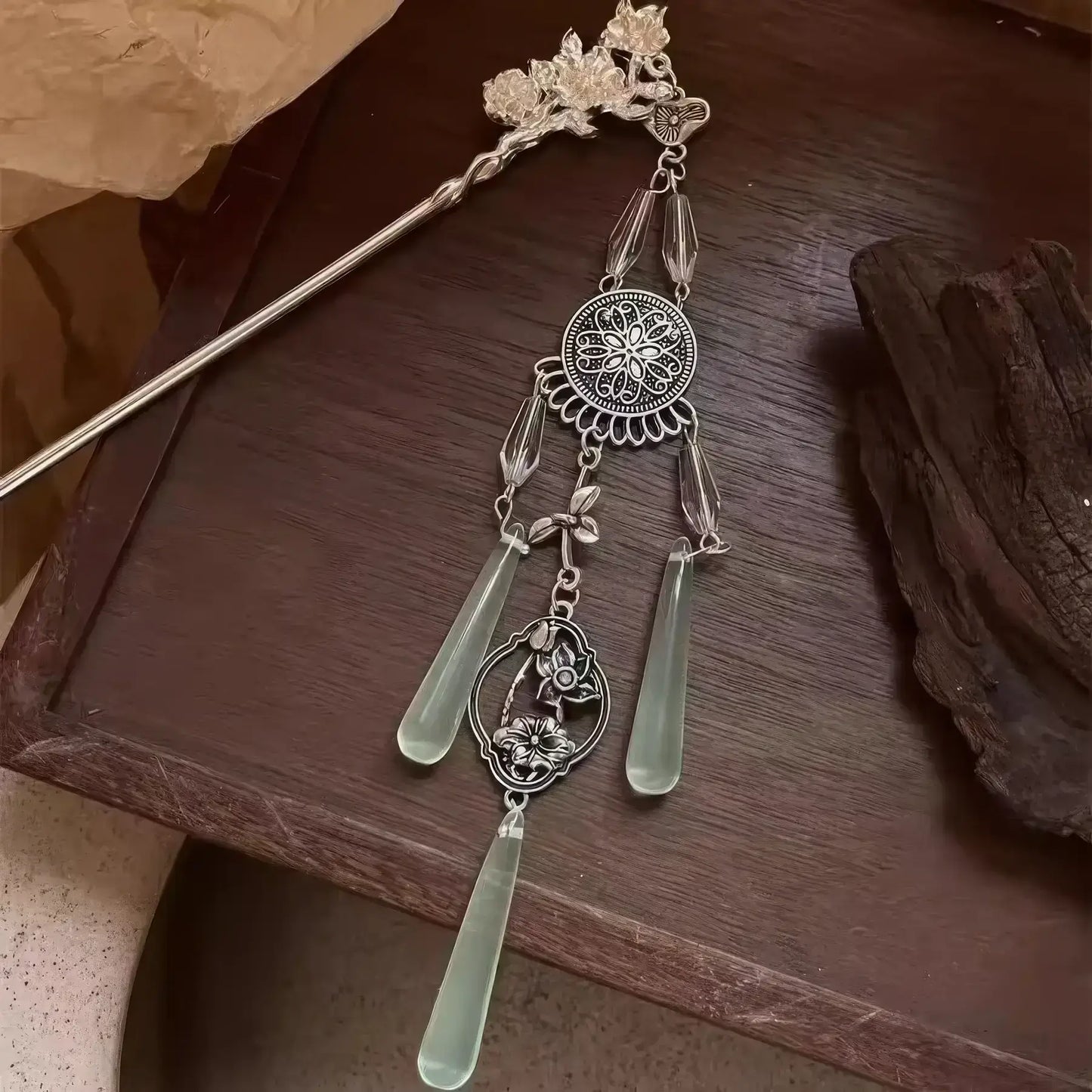 A detailed shot of the retro silver wind chime hairpin displayed on a dark wooden surface, focusing on the filigree patterns and dangling water drop pendants.
