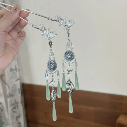 A pair of retro silver wind chime water drop tassel hairpins held in hand, showcasing the intricate silver filigree, wind chime details, and jade-green water drop tassels.