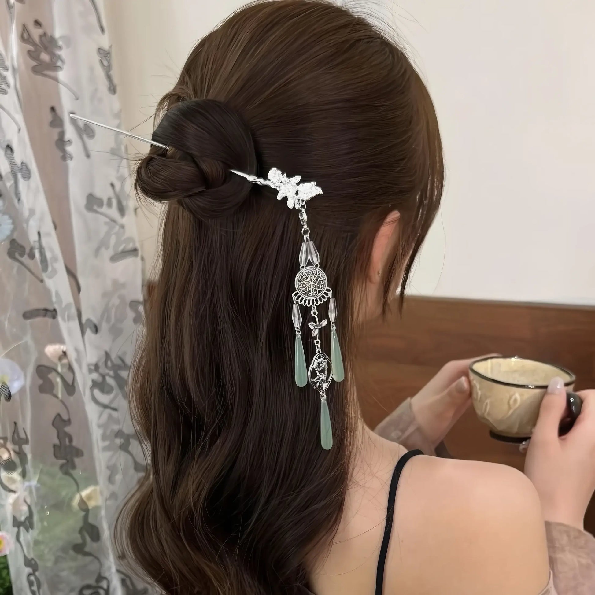 The retro silver wind chime hairpin worn in a half-up hairstyle, shown from the back view, with the wearer holding a teacup.