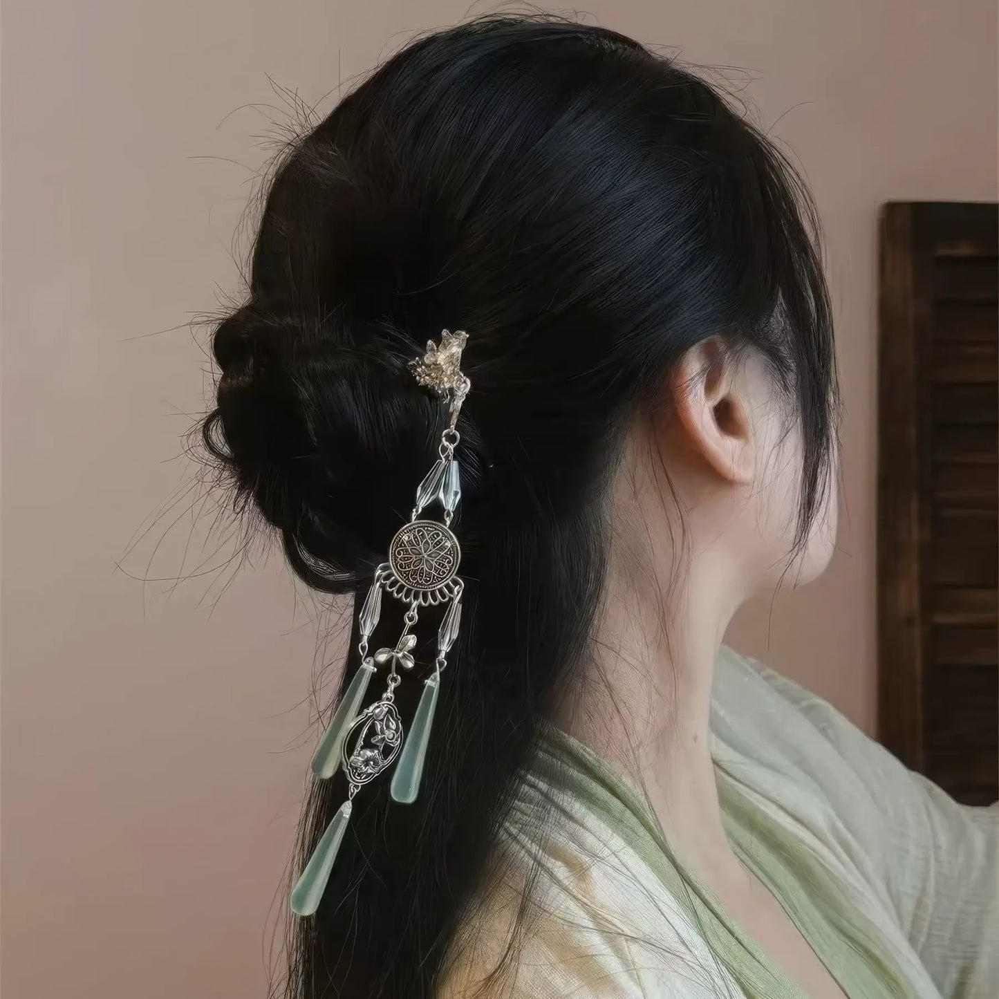 A retro silver wind chime water drop tassel hairpin worn in a neat traditional bun, shown from the side view, paired with a light green hanfu.