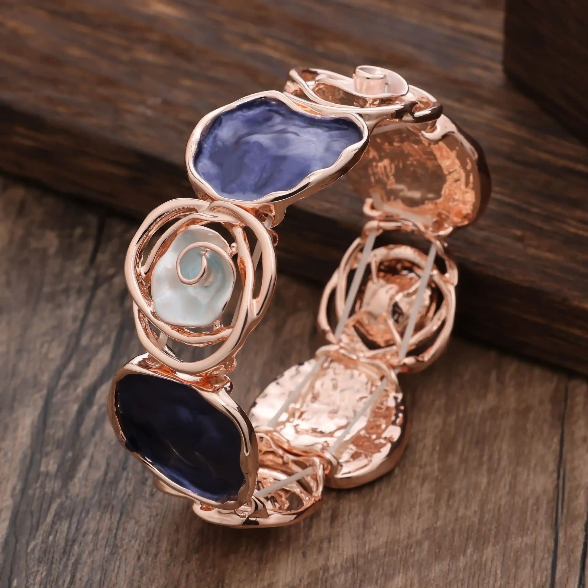 Rose - themed bracelet in rose gold featuring dark - colored stones, placed on a wooden surface.