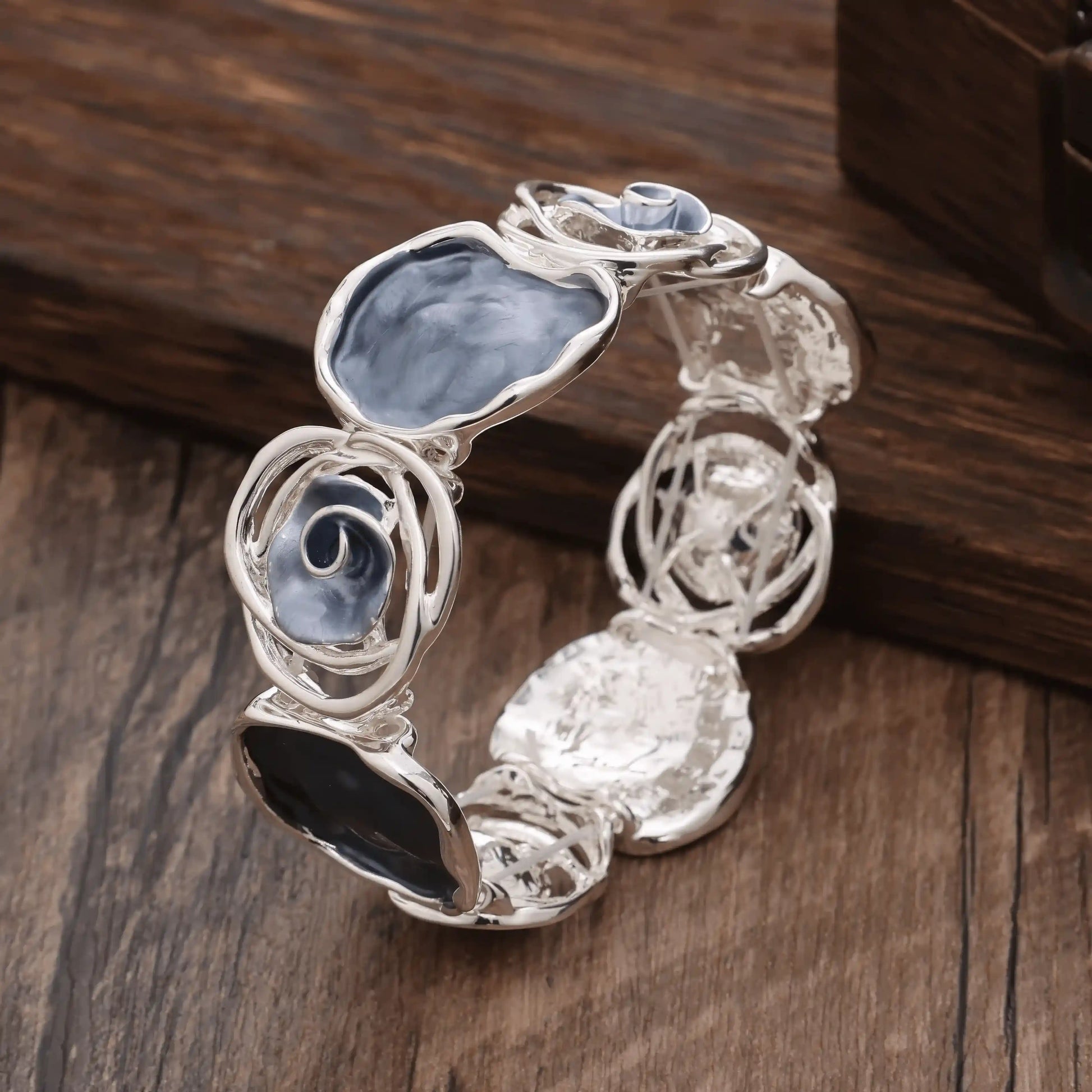 Rose - themed bracelet in silver with blue and black stones, placed on a wooden surface.