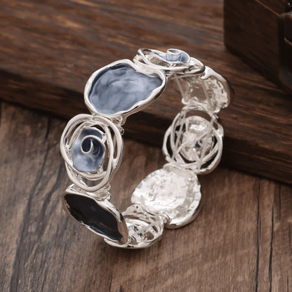 Rose - themed bracelet in silver with blue and black stones, placed on a wooden surface.