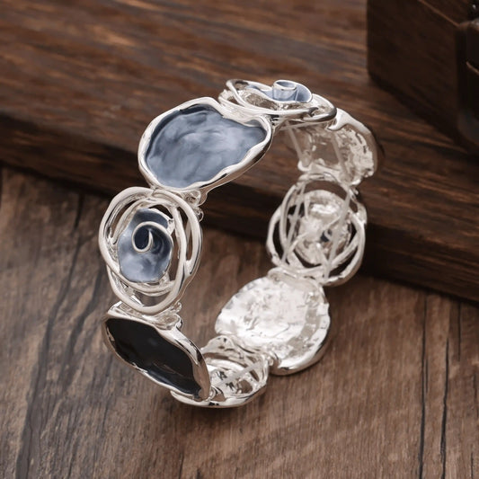 Rose - themed bracelet in silver with blue and black stones, placed on a wooden surface.