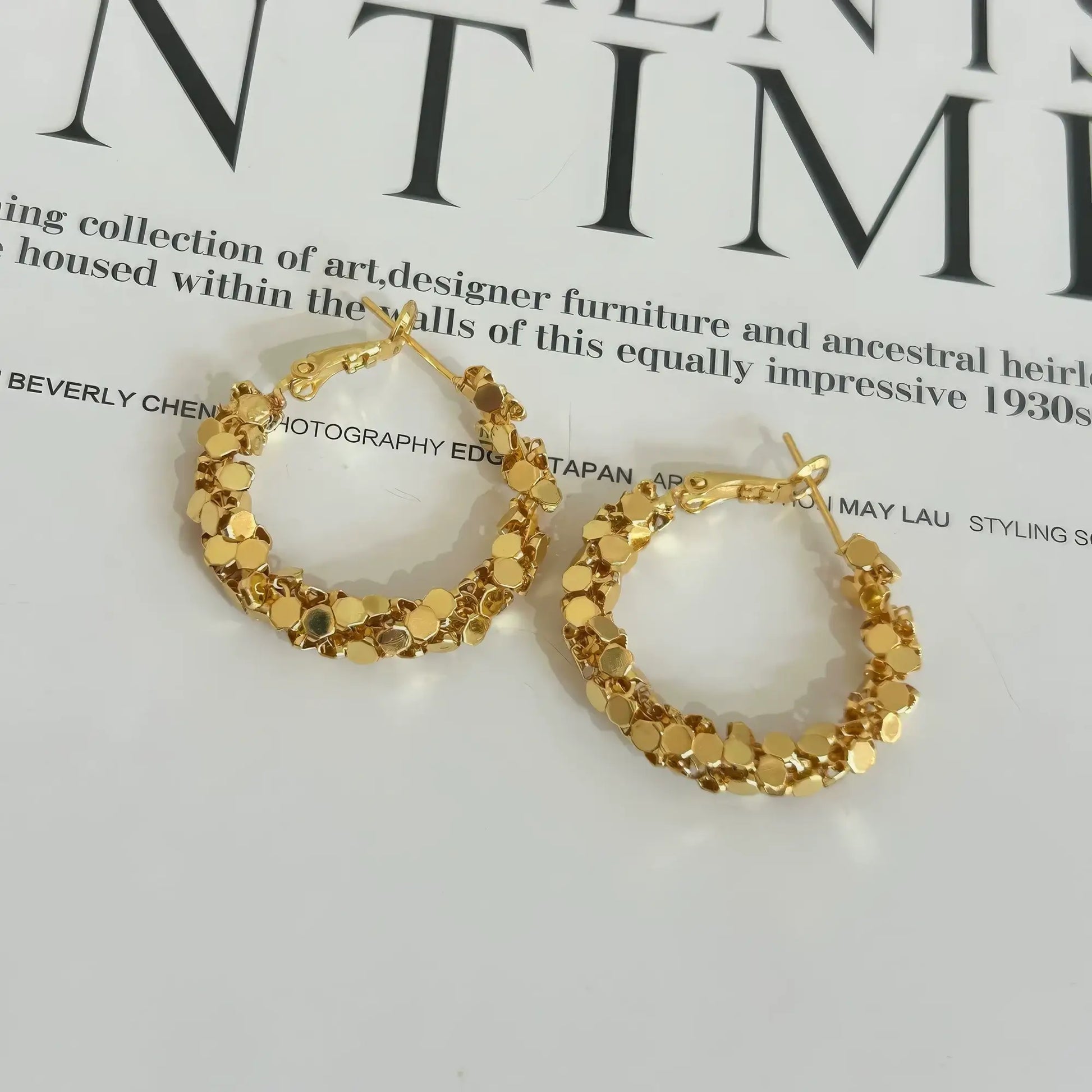 Pair of gold sequined hoop earrings displayed on a magazine, highlighting the textured, sparkling design