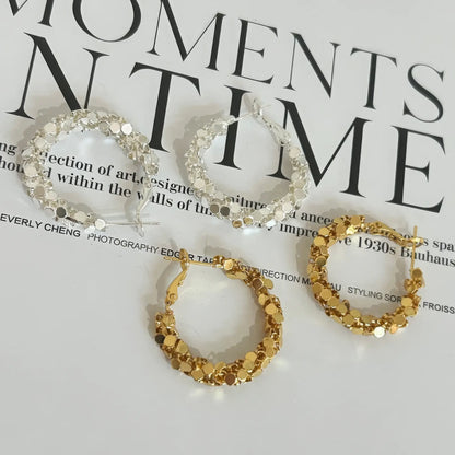  Mixed gold and silver sequined hoop earrings displayed on a magazine, showcasing the contrast of metallic tones