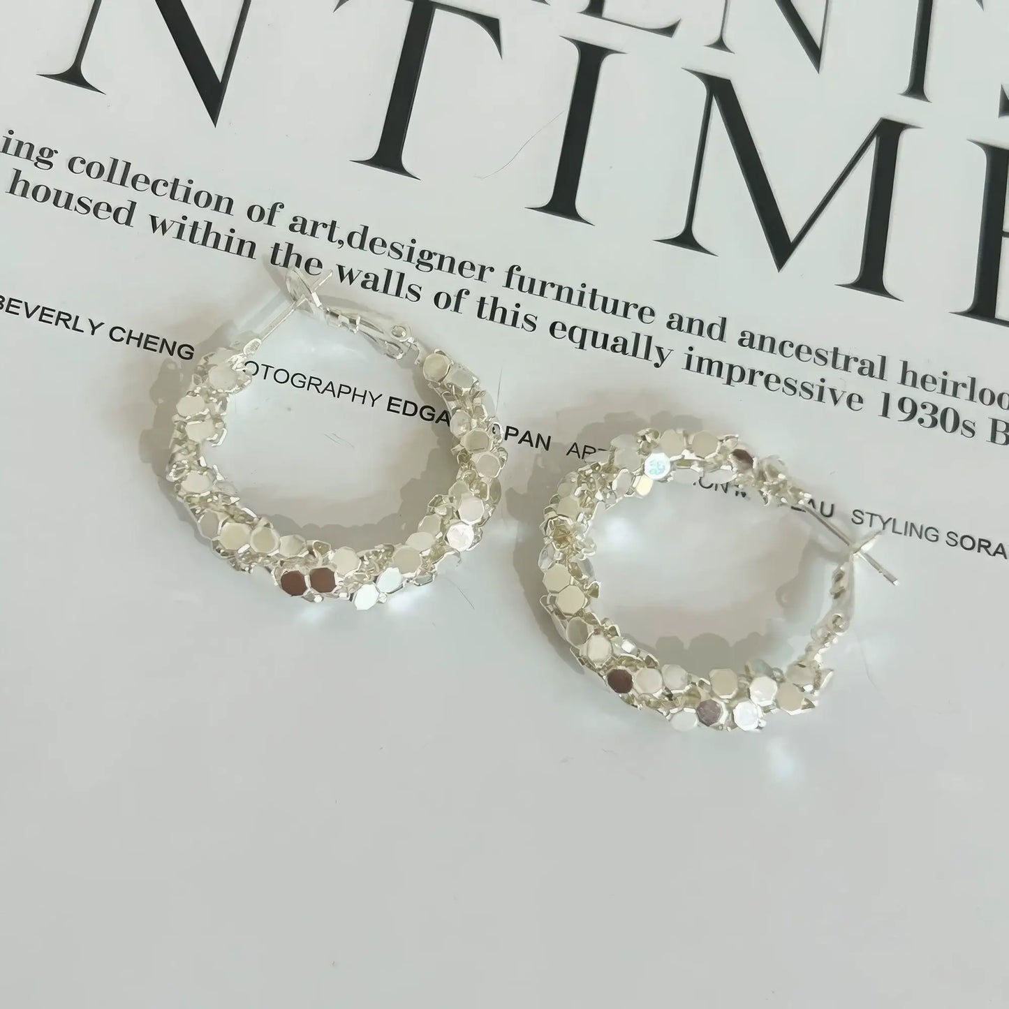 Pair of silver sequined hoop earrings displayed on a magazine, emphasizing the sparkling, segmented design