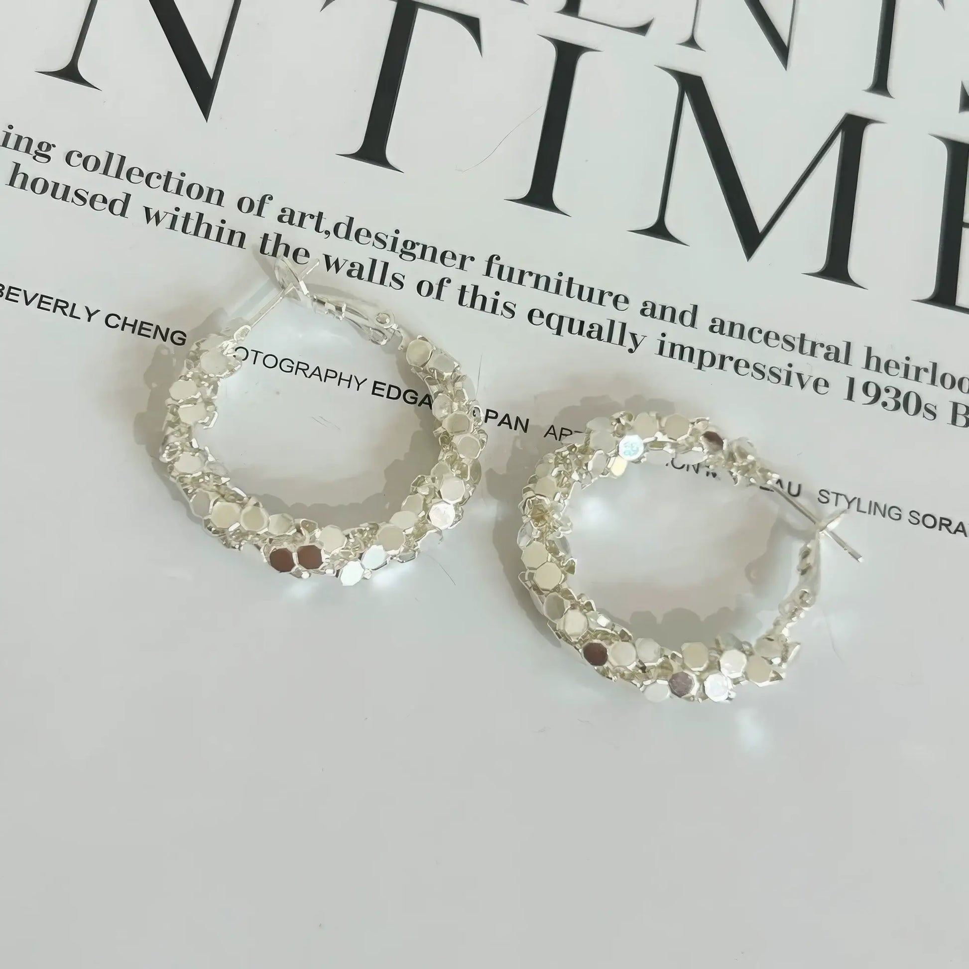 Pair of silver sequined hoop earrings displayed on a magazine, emphasizing the sparkling, segmented design