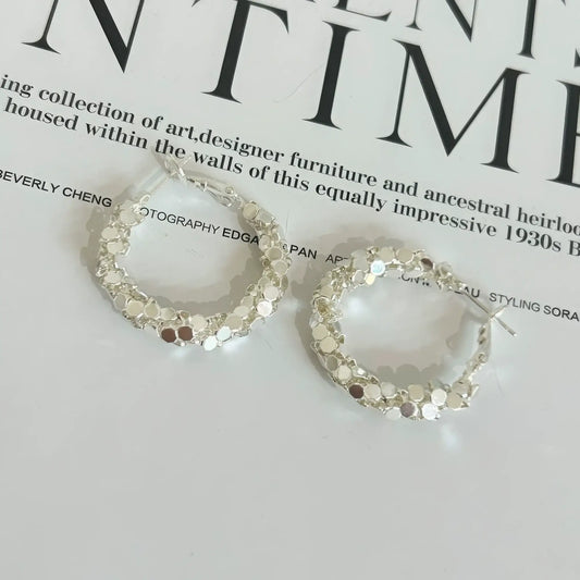 Pair of silver sequined hoop earrings displayed on a magazine, emphasizing the sparkling, segmented design