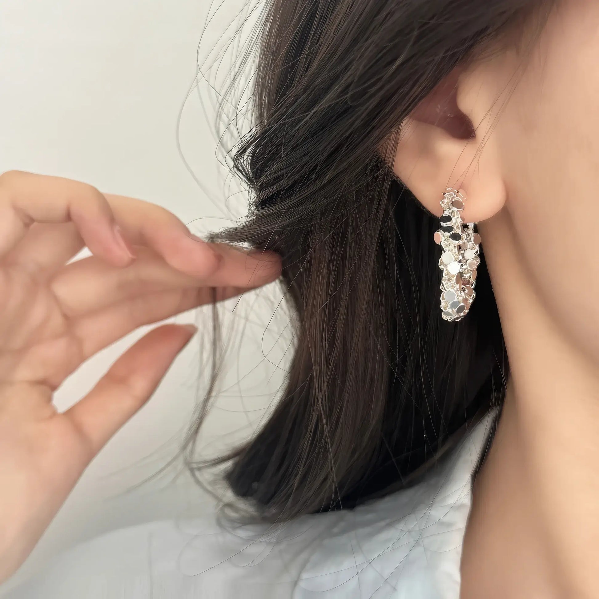  Silver sequined hoop earring worn, hand adjusting hair, highlighting the shiny, textured structure