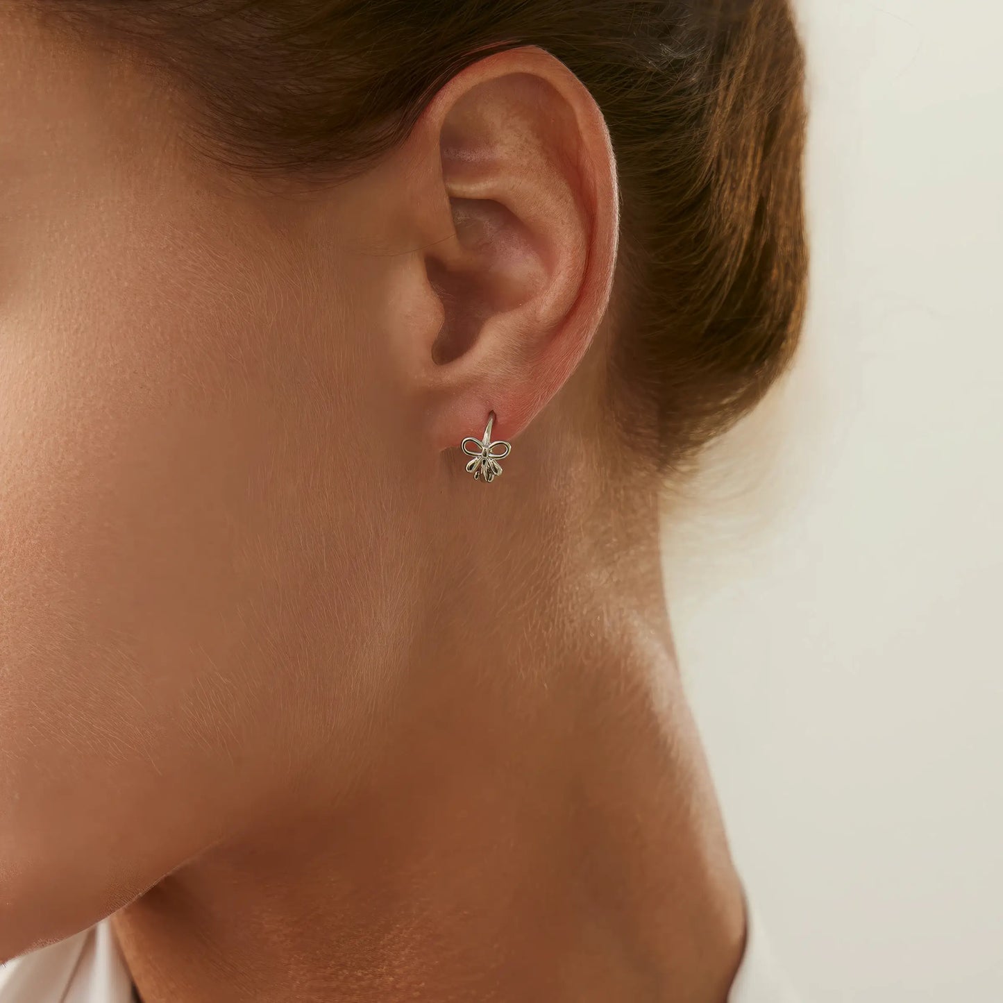 Silver bow tie stud earring worn on ear, showing a delicate and charming style.