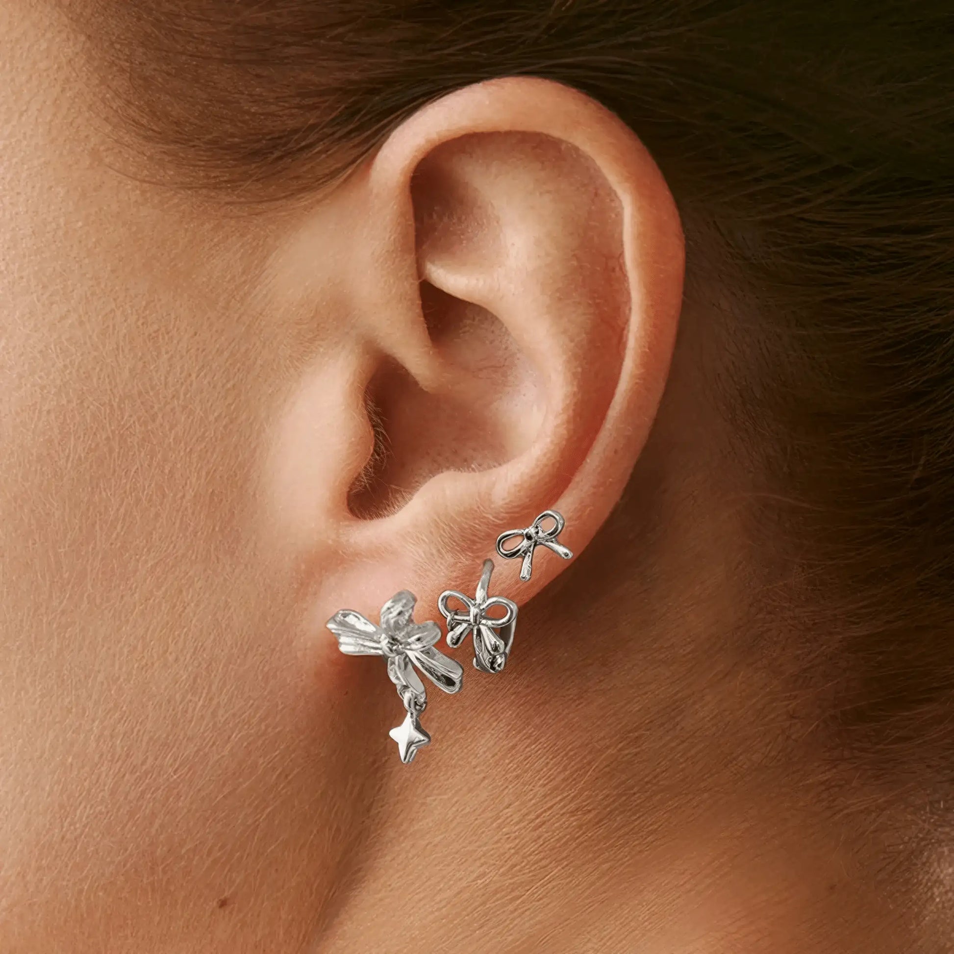 Set of silver bow tie stud earrings worn on ear, displaying a fashionable look.