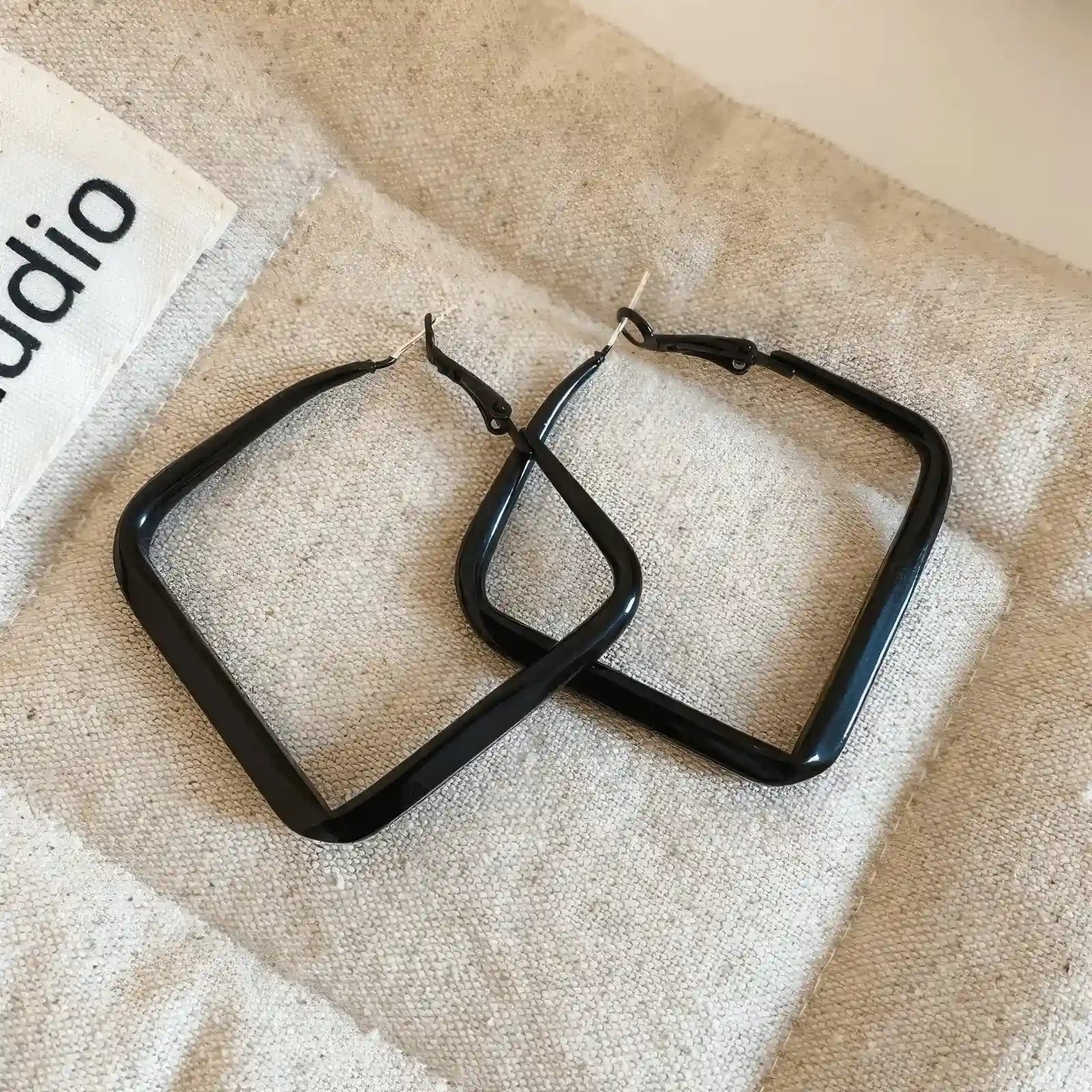 Pair of black silver needle spray - painted square geometric earrings, displayed on fabric, showcasing the sleek, square structure