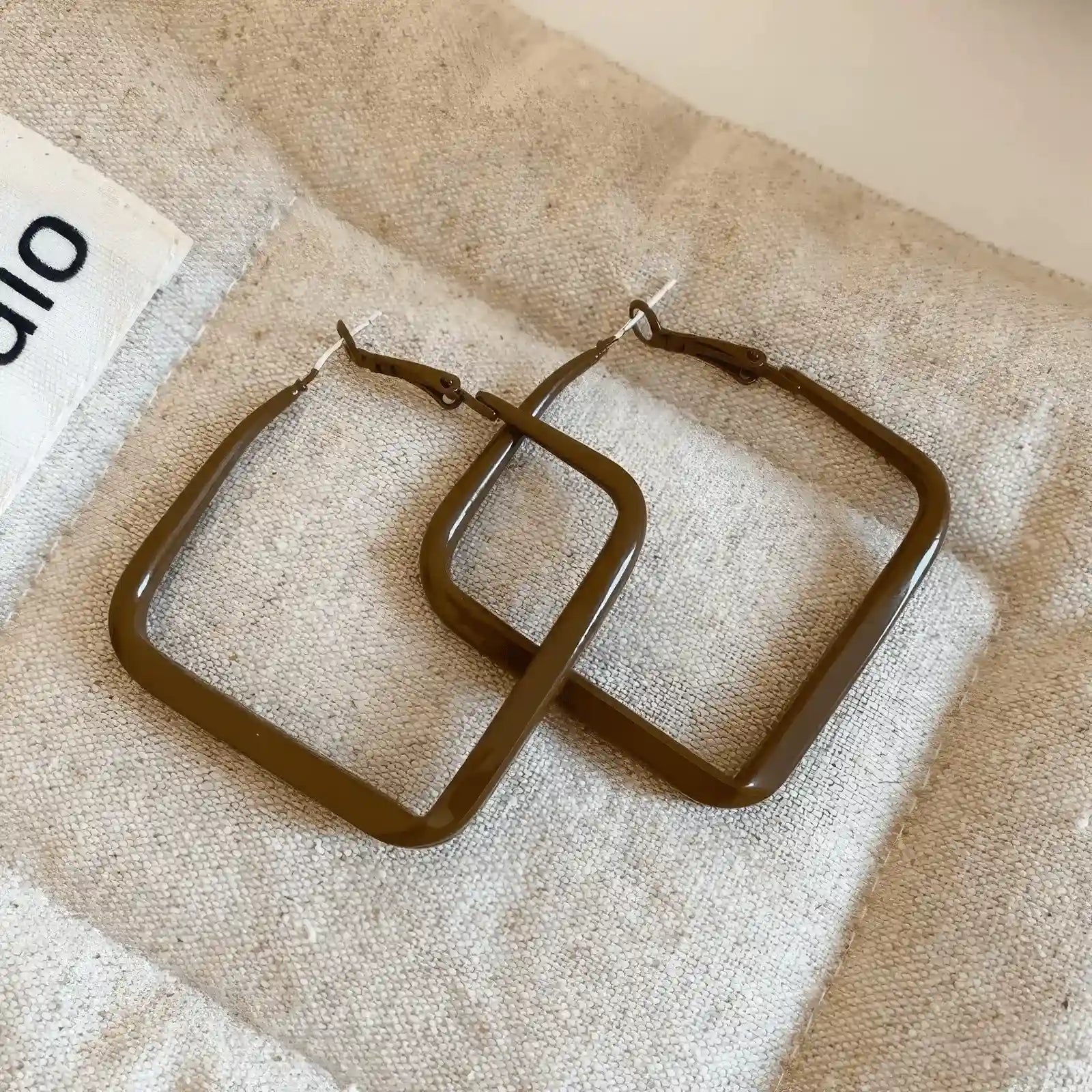 Pair of brown silver needle spray - painted square geometric earrings, displayed on fabric, emphasizing the stylish, square design