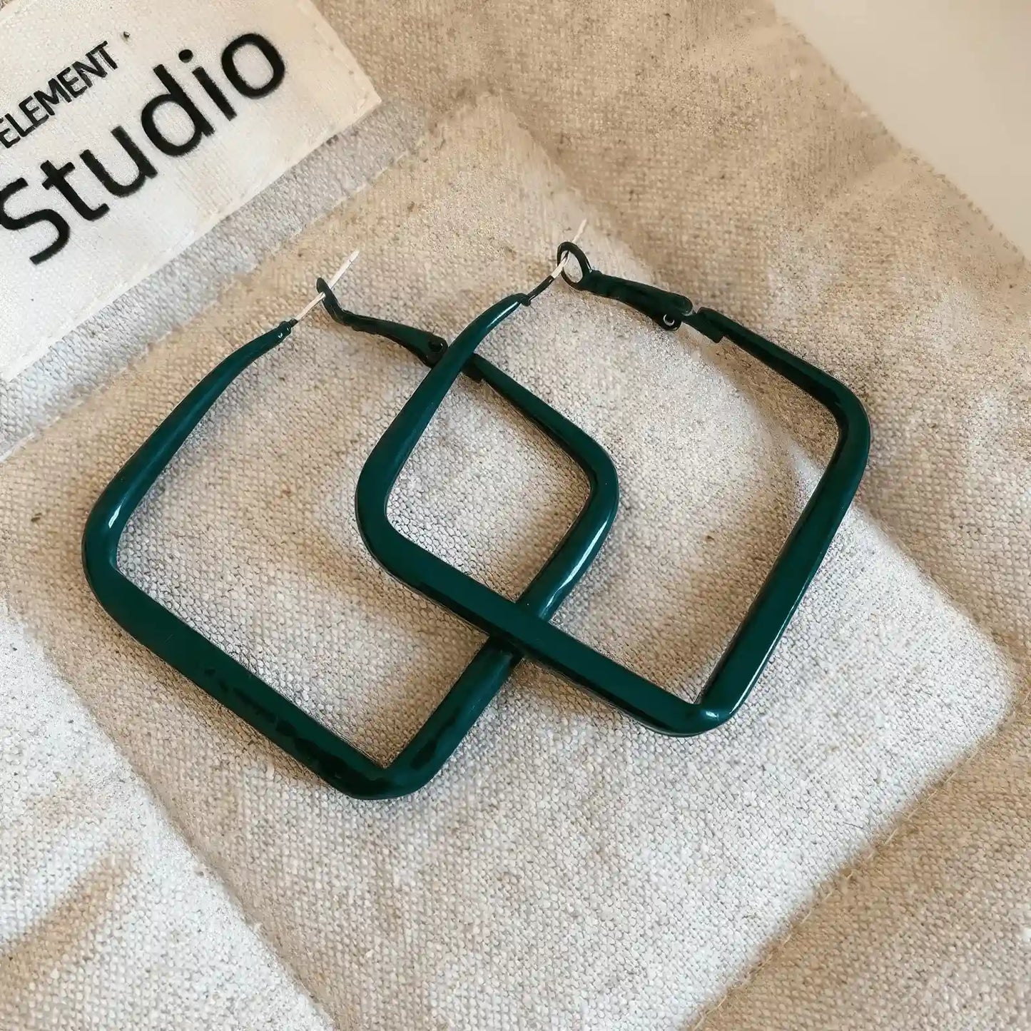 Pair of green silver needle spray - painted square geometric earrings, displayed on fabric, highlighting the sleek, square structure